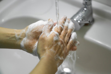 Washing hands with soap under the faucet with water.