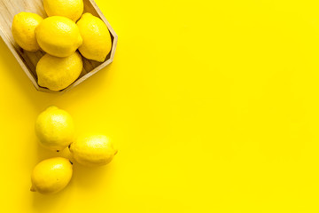 Ripe lemons in tray on yellow backgroud top-down frame copy space
