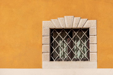 Small window with wrought iron security bars on an orange and white wall. Trentino Alto Adige, Italy, Europe