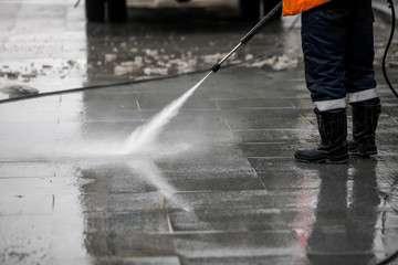 Worker cleaning driveway with gasoline high pressure washer splashing the dirt, asphalt road...