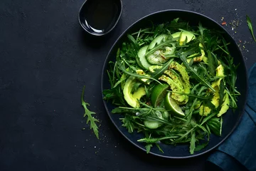 Poster Green vegetable salad with arugula, cucumber and avocado. Top view with copy space. © lilechka75