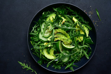 Green vegetable salad with arugula, cucumber and avocado. Top view with copy space.