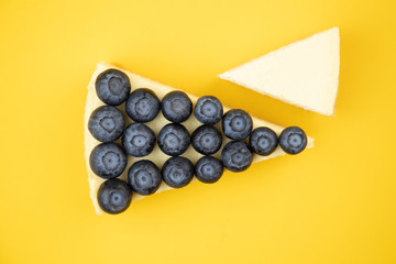 Slice of blueberry cheesecake on a yellow background. Minimalistic composition.