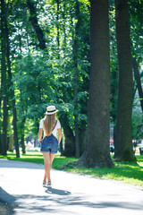 young beautiful girl in denim overalls and a light hat walking in the park