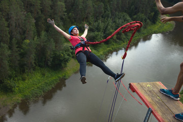 Young woman, tethered to a safety rope, falls from a great height into a deep canyon on the background of a river, close-up. Ropejumping.