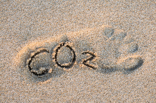 Eco-friendly carbon footprint message with handwritten CO2 text in the outline of a foot on a grainy golden sand beach