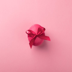 Bright pink egg with a satin bow on a pink background. Festive spring concept. Color trend. Selective focus close-up.