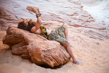 Caveman reclining alone with his primitive stone tablet outdoors in a weathered rock cave