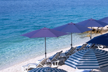 Blue beach umbrellas and chaise for relax on sea resort. Summer vacations and travel for seaside. Paid service on comfort beaches. Сopy space for text.