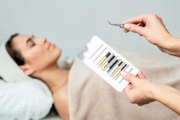 Beautician holds eyelashes by tweezers.