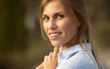 Attractive young blond woman close-up portrait. Female outdoors on spring sunshine background. Cheerful lady closeup portrait in fall time.