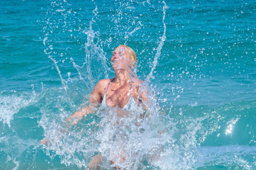 A  woman having fun in the waves of the sea which are splashing her. The beautiful woman (mother of three) in bikini