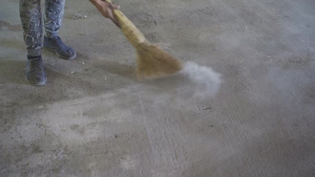 Worker sweeping dusty concrete floor
