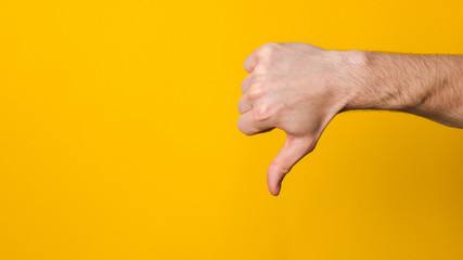 Naklejka premium not good and not approved. close up hand of a man showing thumb down dislike sign over yellow background with copyspace for design