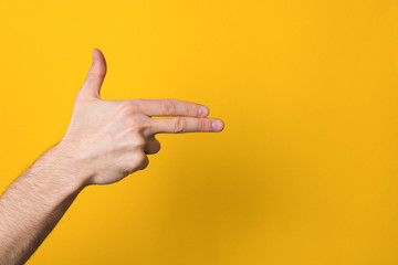 man hand imitating gun over a wide yellow background with copyspace