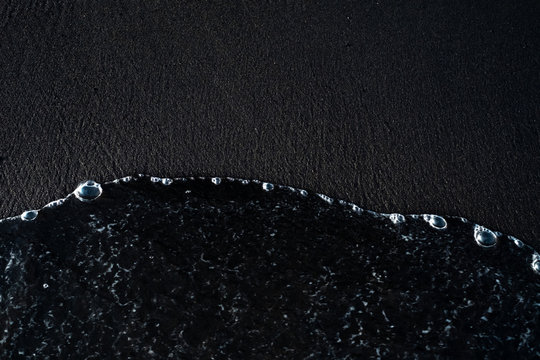 Beach With Black Volcanic Sand And Wave Foam On The Coast Of Bali