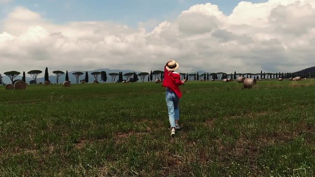 Slow motion video of young caucasian woman running on field in rural area making stop for clocking photos of beautiful landscape, excited hipster girl enjoying nature and recreate on meadow