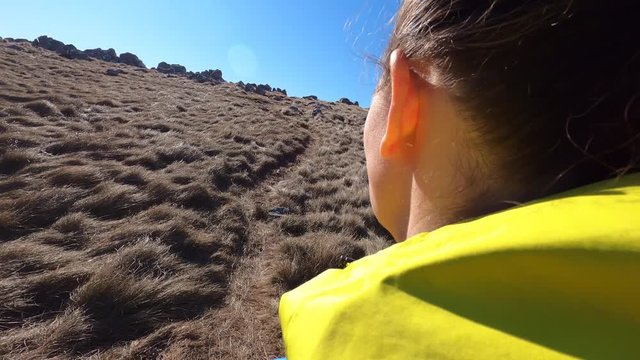TS Female hiker walking up a mountain on a narrow grassy path in sunshine