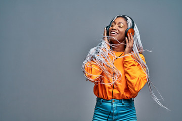 Portrait of adorable girl happy smiling during photoshoot. Stunning african woman relaxing in headphones and funny dancing on gray background.