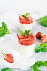 Delicious italian dessert panna cotta  with strawberry sauce, strawberries and fresh mint leaves. Summer creamy dessert with berries and mint in a glass on a light background.