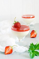 Delicious italian dessert panna cotta  with strawberry sauce, strawberries and fresh mint leaves. Summer creamy dessert with berries and mint in a glass on a light background.