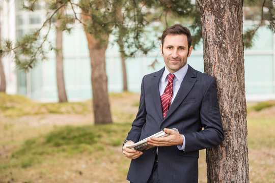Businessmann lehnt am Baum vor Businessgeb&auml;ude