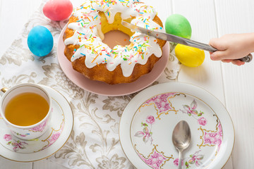cutting an easter cupcake, tea, cream, colorful eggs on a white table, easter food concept