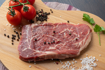 Raw beef steak with spices on a dark board. View from above.