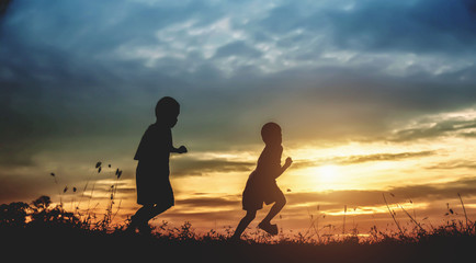 Silhouette, group of happy children playing on meadow, sunset, summertime