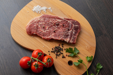 Raw beef steak with spices on a dark board. View from above.