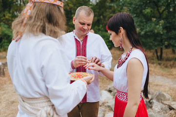 The wedding ceremony of the newlyweds in embroidered clothes, in the old Ukrainian traditions of paganism. Ethnic rite for newlyweds in Ukraine. The bride and groom put on gold rings to each other.