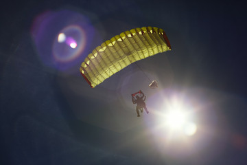 Parachute tandem under a bright canopy of a parachute with solar lens flare against the background of a dark blue sky, close-up. Parachute jumping.