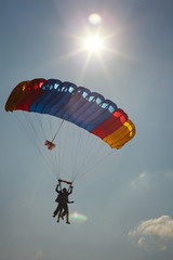 Silhouettes of instructor and passenger under the canopy of a parachute during a tandem jump against the background of the sun and blue sky, close-up. Parachute jumping.