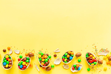 Fototapeta na wymiar Chocolate Easter eggs and colorful candies on yellow paper background. flat lay, copy space, top view, overhead, template, mockup