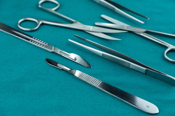 Basic surgical instrument scalpel forceps tweezers scissors spread on surgical green drape fabric