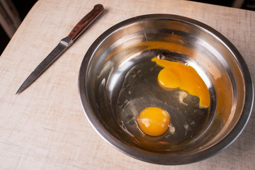 Egg in a glass bowl and egg shells on wooden table. Baking ingredients, top view