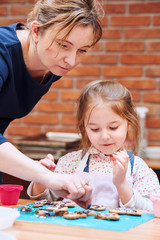 Fototapeta premium Little girl with her mom's help decorating baked cookies with colorful sprinkle and icing sugar. Kid taking part in baking workshop. Baking classes for children, aspiring little chefs