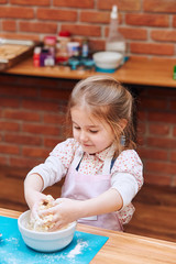 Little girl kneading the dough for baking the cake. Kid taking part in baking workshop. Baking classes for children, aspiring little chefs. Learning to cook. Combining and stirring prepared ingredient