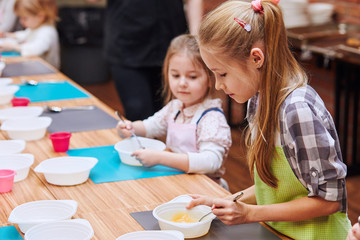 Little girls stirring the yolk with sugar. Kids taking part in baking workshop. Baking classes for children,  aspiring little chefs. Girls learning to cook. Combining and stirring prepared ingredients