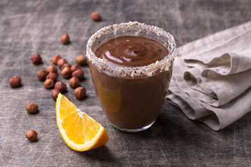 Chocolate mousse with cream, hazelnuts and orange in glasses on old dark wooden table.