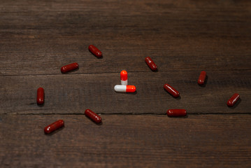 Red-white and brown capsule pills scattered on a wooden background. Antibiotics