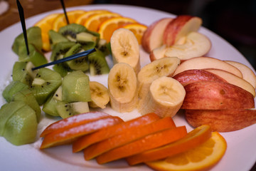 Sliced ​​banana, orange, apple and kiwi on a white plate. Tasty and healthy food. Close-up photo.