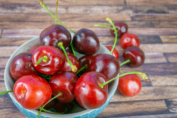 Fresh sweet cherries in a cup, dark brown wood background with copy space