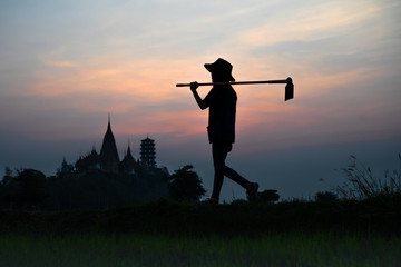 silhouette of farmer walks carry hoe to the rice fiels in the early morning, living life of Thai...