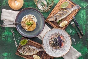 cooked dorado, trout, seafood pasta and fish patties and glass of white wine on green background