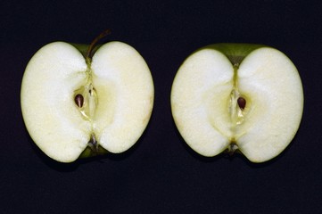 Two halves of a green juicy sliced ​​apple on black background