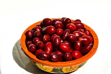 Dark red dogwood berries in wooden bowl on white background. Selective focus.  Wooden bowl is painted with old Khokhloma decorative painting. Bunch of attractive oblong ripe dogwood berries. Calmness.