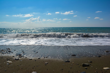 Fototapeta na wymiar a sea wave with foam rolls on a sandy beach on a clear day