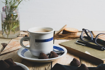 Cup of coffee next to some notes and a pen on a rustic aged wooden table. Empty copy space for Editor's text.