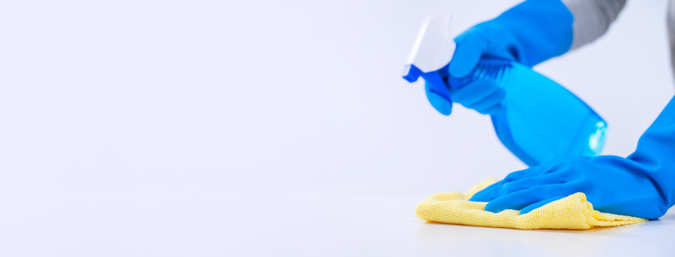Young woman housekeeper is doing cleaning white table in apron with blue gloves, spray cleaner, wet yellow rag, close up, copy space, blank design concept.
